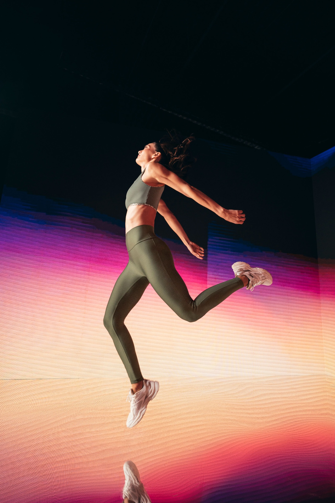 Female athlete mid-jump against a gradient LED wall