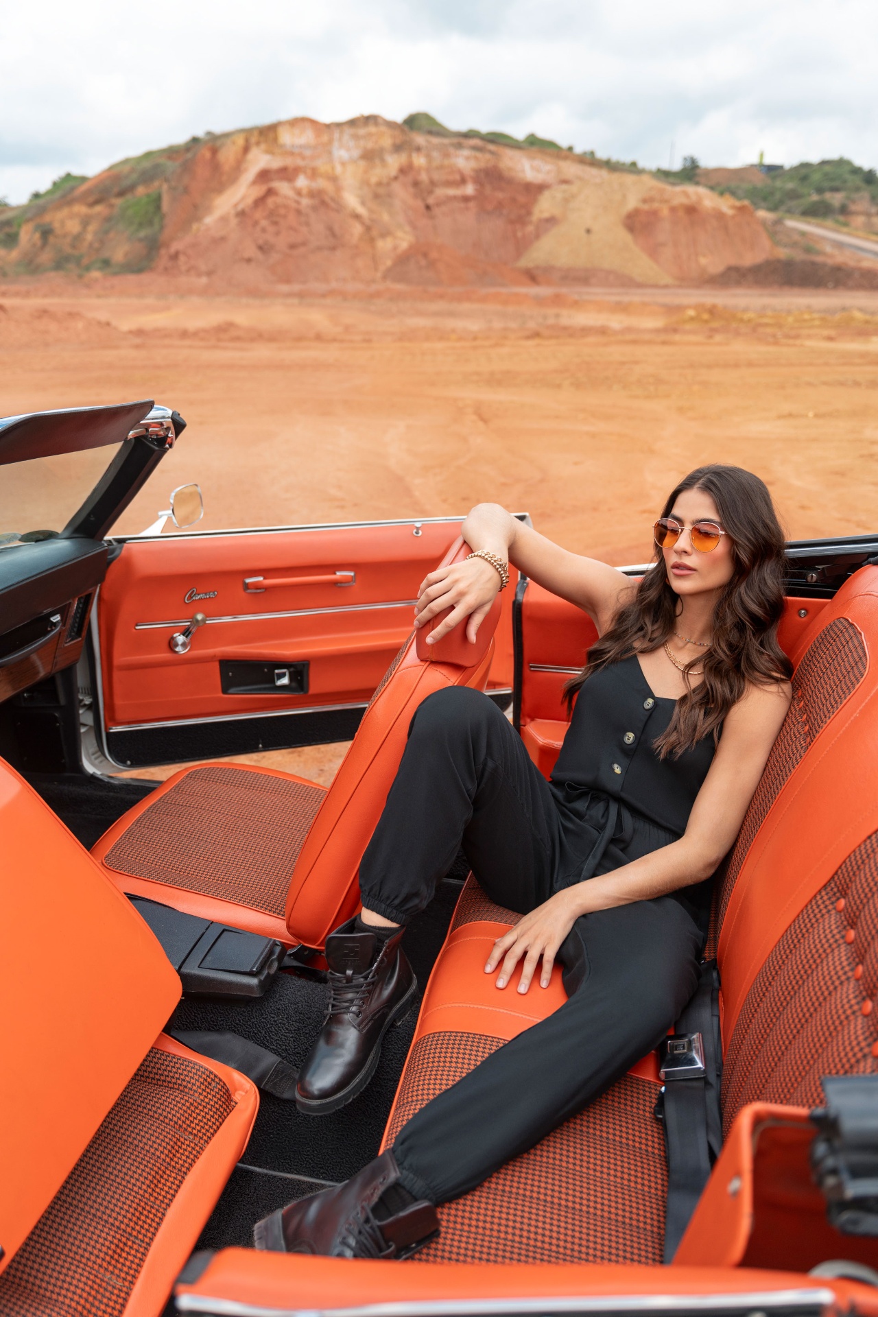 Model reclined inside vintage orange Camaro convertible in desert