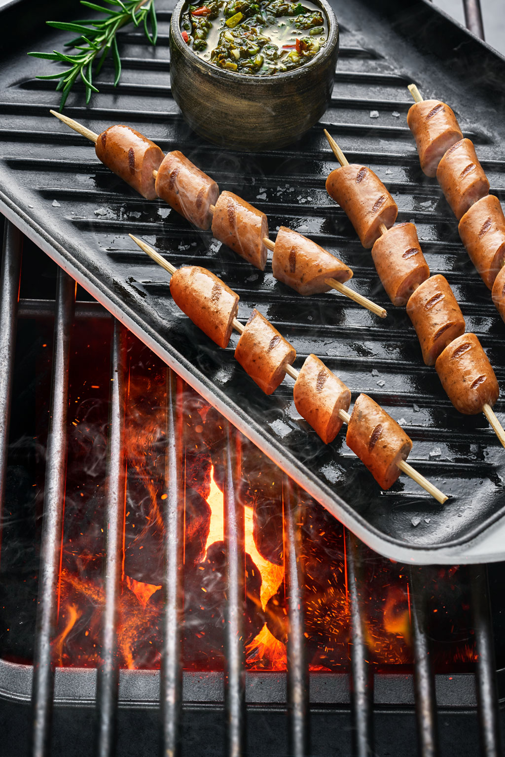 Grilled sausage skewers over embers with chimichurri