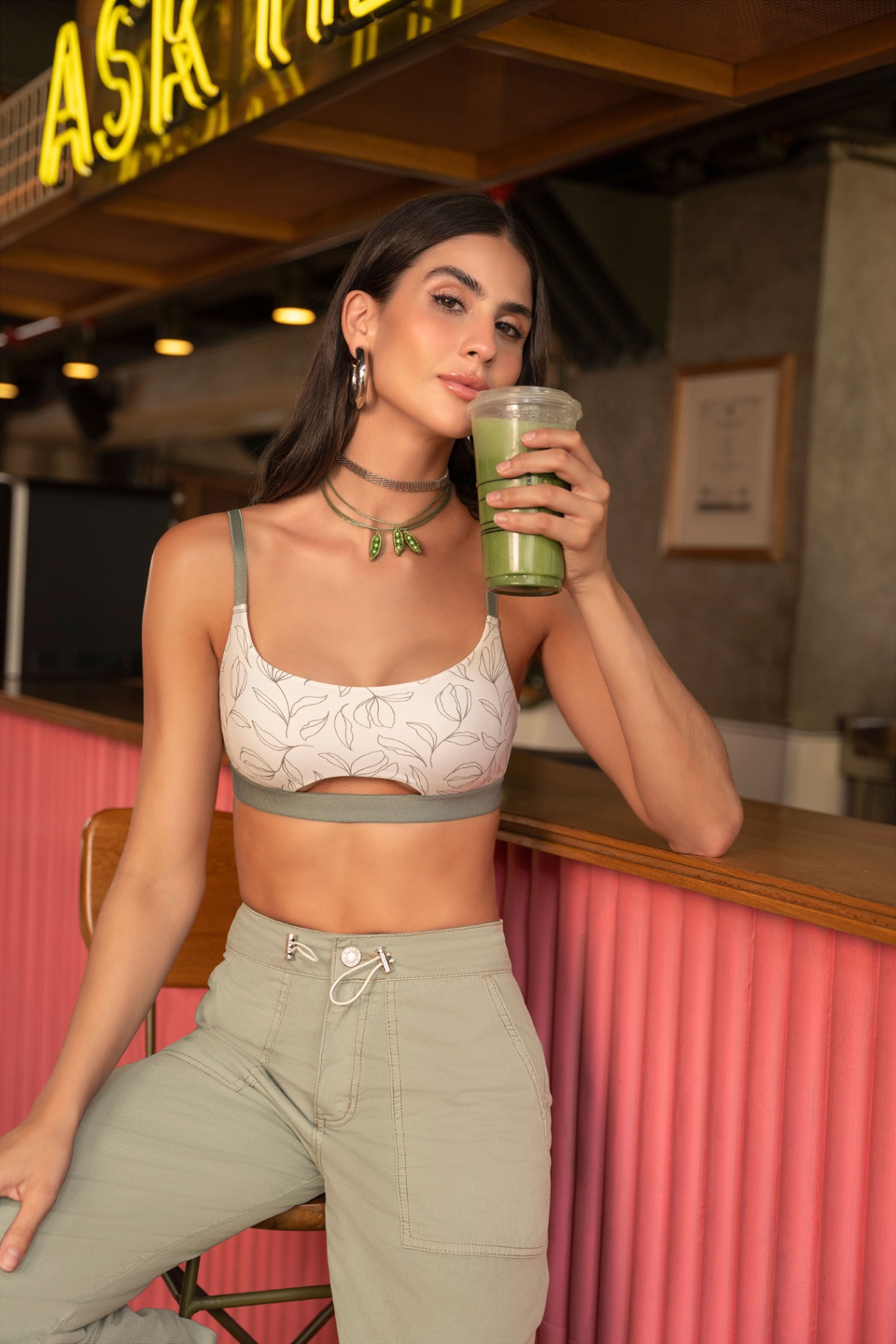 Woman in activewear holding matcha drink under ASK HERE neon