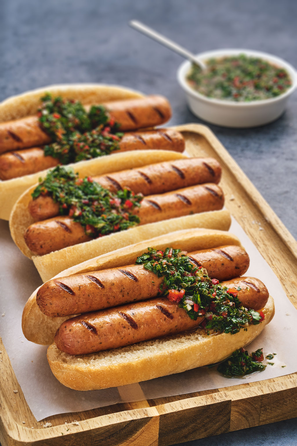 Grilled choripanes with chimichurri on wooden tray