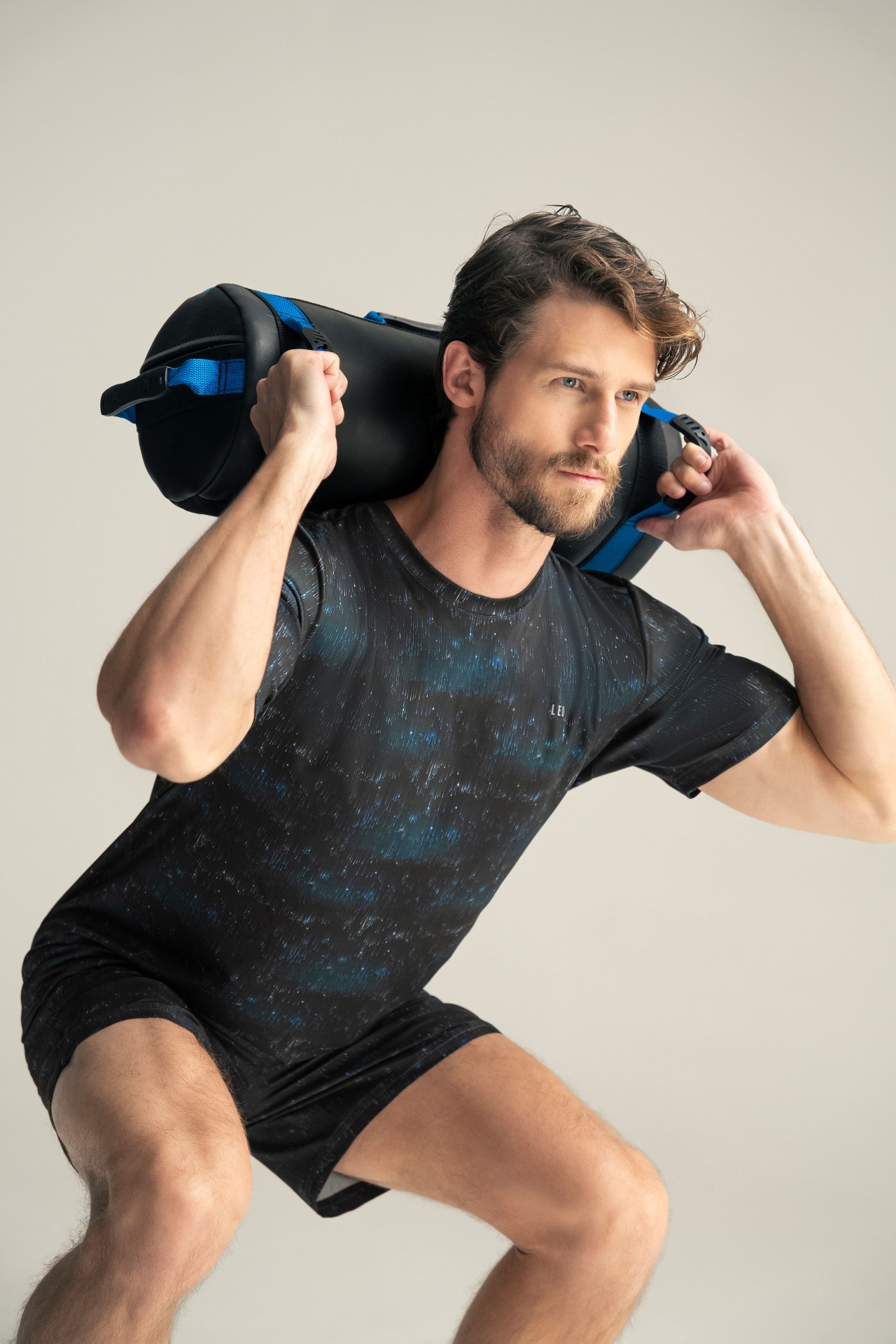 Male athlete lunging with sandbag on studio backdrop