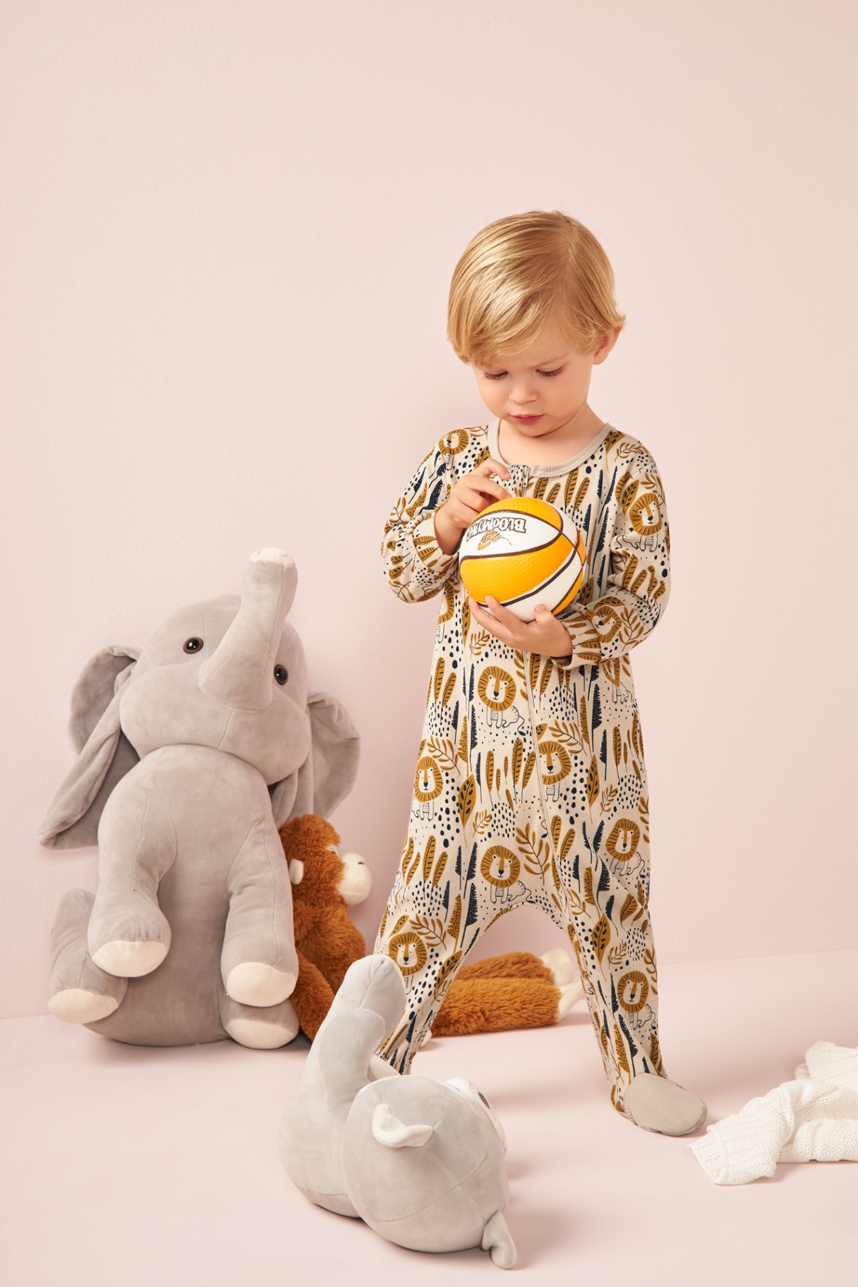Toddler in printed onesie with plush toys on pink set