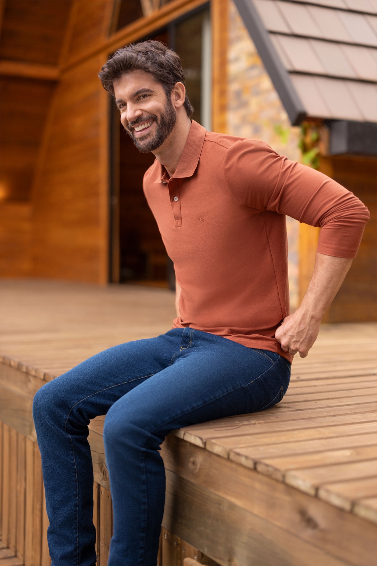 Man in terracotta polo smiling on wooden deck